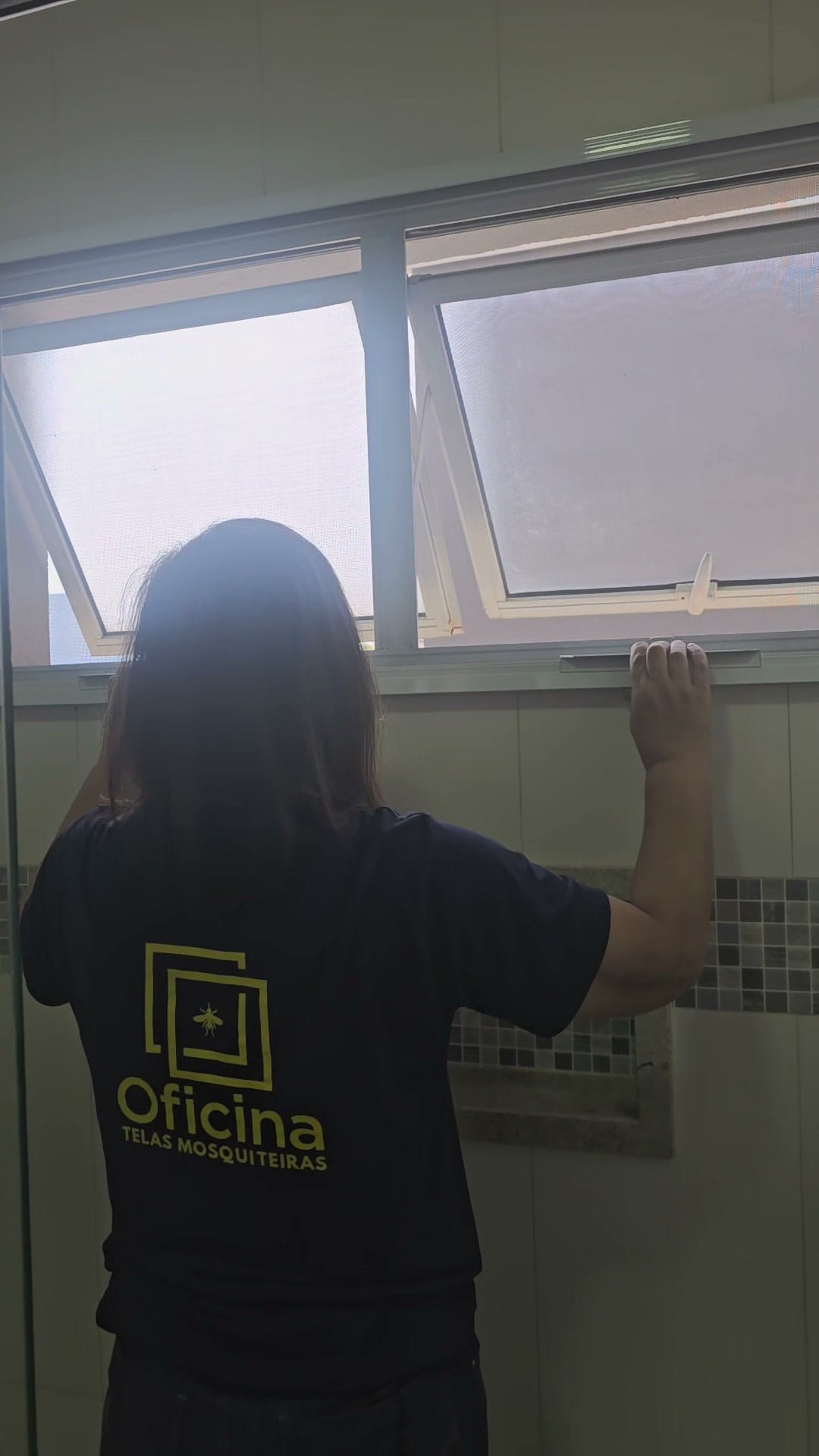 Instaladora da Oficina Telas Mosquiteiras levantando a tela guilhotina para alcançar o puxador da janela maxim-ar