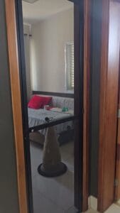 Porta de tela com malha pet em esquadria de alumínio preto, fechada no vão de um quarto