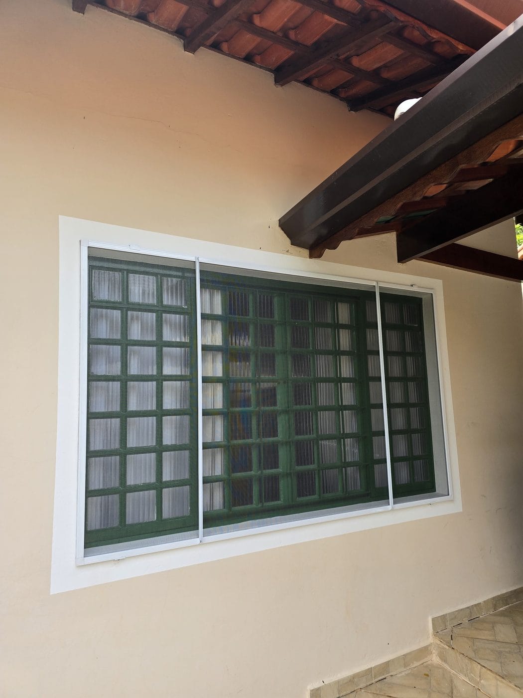 Janela de vidro canelado verde sob telhado de barro em Águas de São Pedro, com tela mosquiteira instalada por dentro
