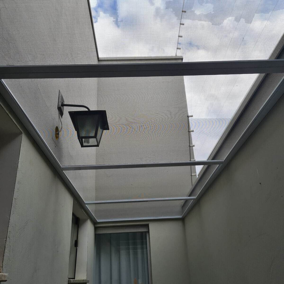 Corredor coberto em Americana com telhado de vidro e tela mosquiteira instalada no vão da própria cobertura