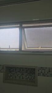 Duas janelas maxim-ar de alumínio branco com tela mosquiteira modelo guilhotina instalada, vistas de dentro do banheiro