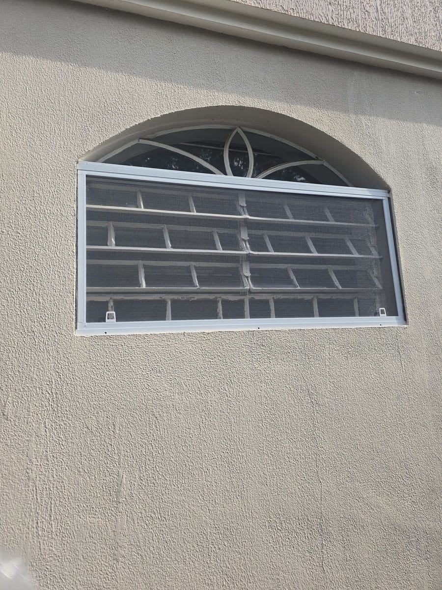 Janela em arco com grade decorativa de ferro e tela mosquiteira instalada por dentro do vão, em parede bege