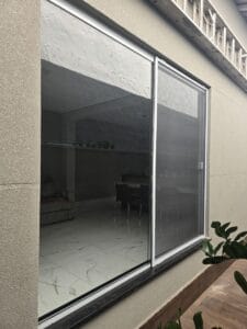 Porta de correr ampla com tela mosquiteira, vista da área externa, mostrando a sala ao fundo