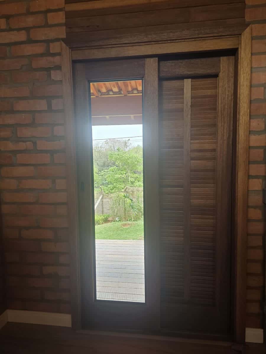 Porta de madeira com tela mosquiteira em parede de tijolo aparente, com vista para o deck e o jardim