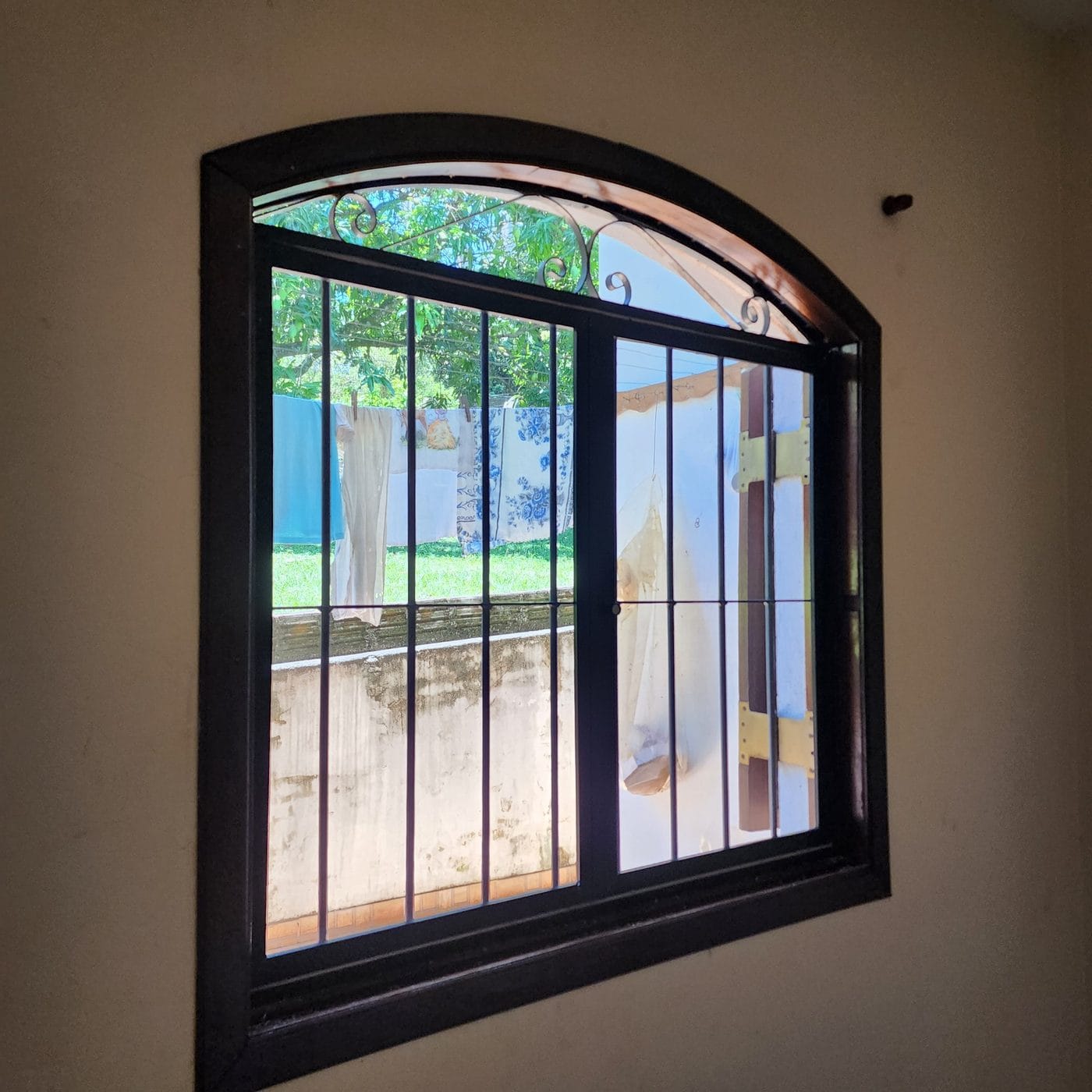 Janela em arco com moldura de madeira escura e ferro trabalhado em São Pedro, com tela mosquiteira instalada e vista para o jardim