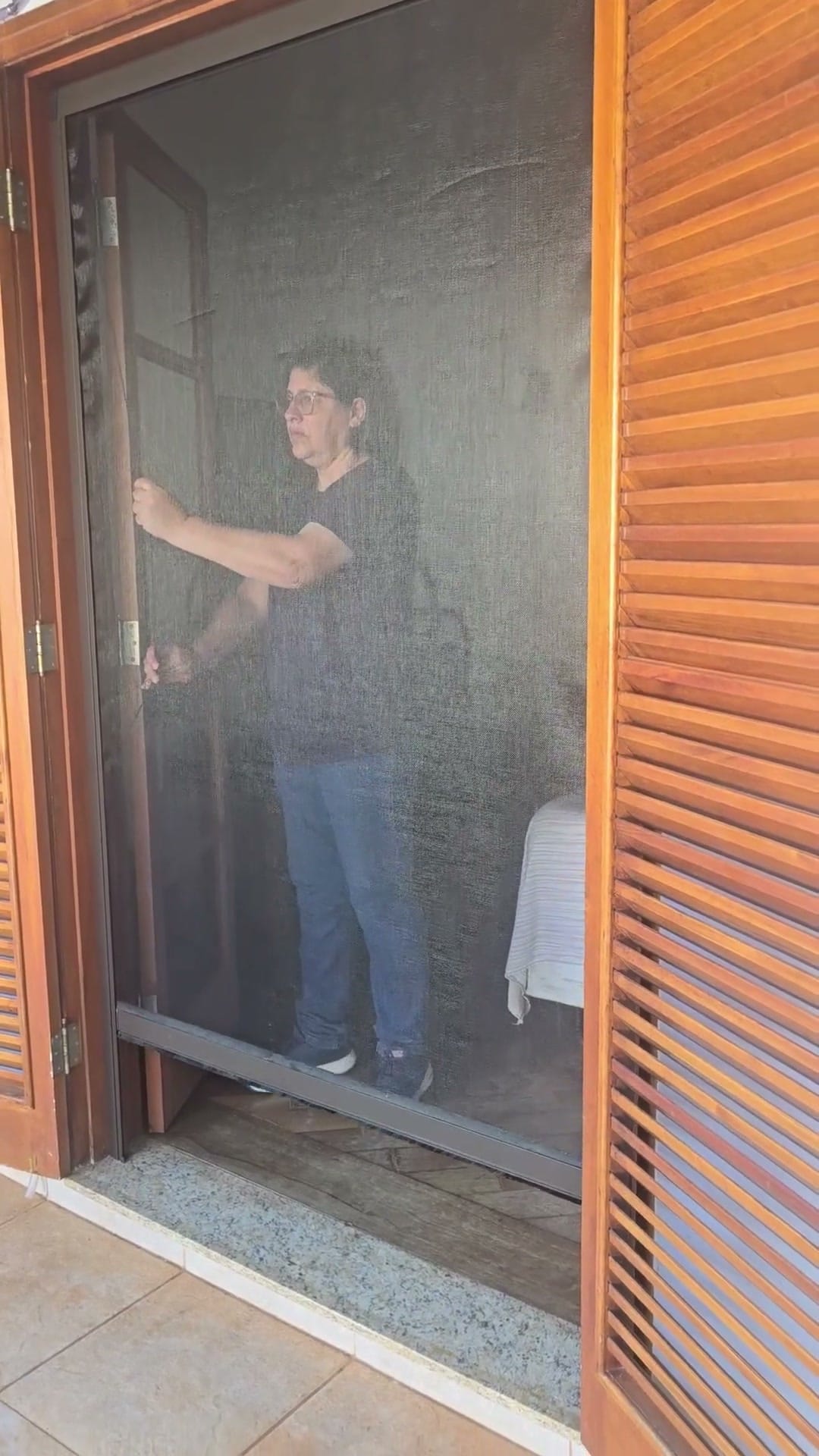 Tela mosquiteira recolhível descida até embaixo numa porta-balcão de madeira com venezianas, em Piracicaba