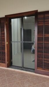 Tela mosquiteira em esquadria de alumínio, duas folhas de giro, fechando uma porta-balcão de madeira com veneziana