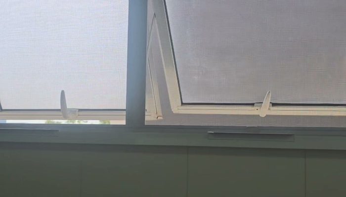 Duas janelas maxim-ar de alumínio branco com tela mosquiteira modelo guilhotina instalada, vistas de dentro do banheiro