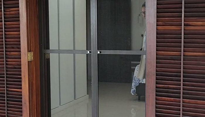 Tela mosquiteira em esquadria de alumínio, duas folhas de giro, fechando uma porta-balcão de madeira com veneziana