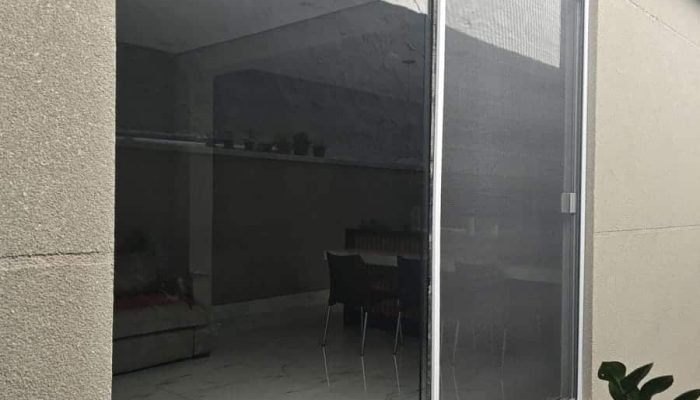 Porta de correr ampla com tela mosquiteira, vista da área externa, mostrando a sala ao fundo