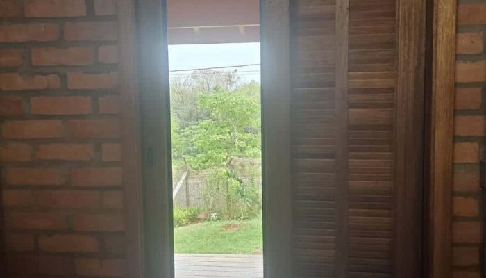 Porta de madeira com tela mosquiteira em parede de tijolo aparente, com vista para o deck e o jardim