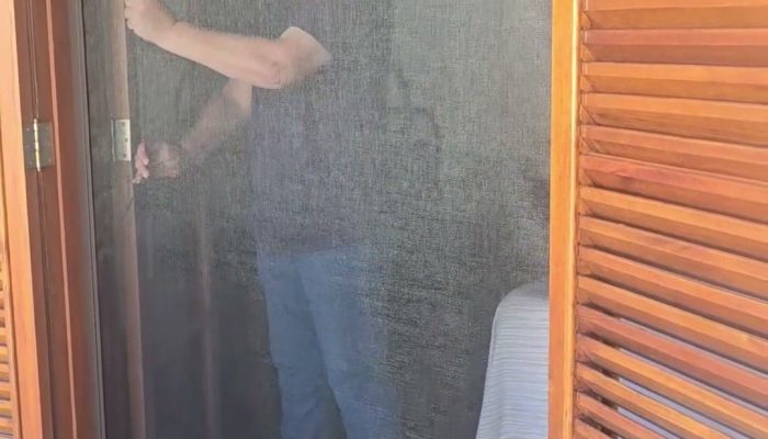 Tela mosquiteira recolhível descida até embaixo numa porta-balcão de madeira com venezianas, em Piracicaba